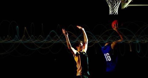 Basketball Players in Intense Competition Under Bright Hoop