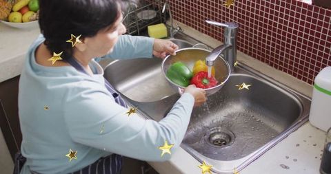 Senior woman rinsing bell peppers in kitchen