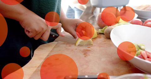 Hands slicing lemon on wooden cutting board with fresh fruit and bowl in daylight