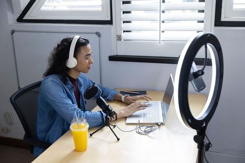 Non-binary creator streaming and typing at home desk with ring light, microphone, laptop