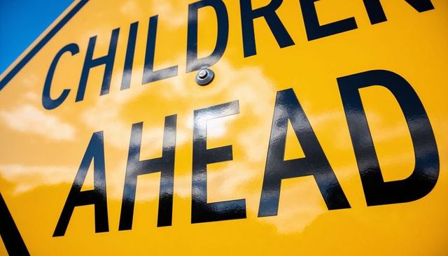 Close-up glossy yellow children ahead road sign with sky reflections and bolt detail