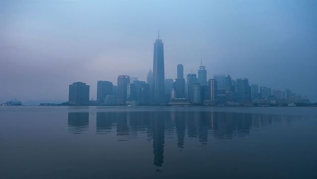 Dramatic dusk skyline with towering central skyscraper reflecting on tranquil harbor