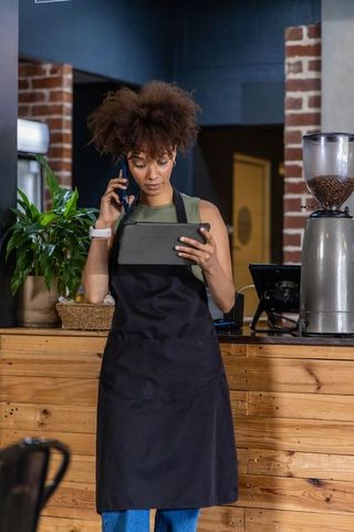 African american barista using tablet while speaking on phone behind cafe counter