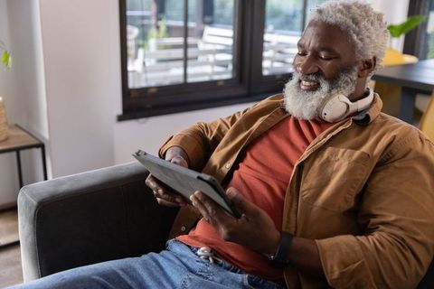 Relaxed african american senior man using tablet on sofa wearing headphones at home