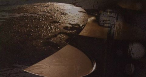 Moody close-up of overlapping metal spoons with water droplets on dark wooden tabletop
