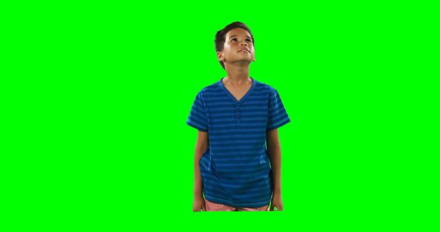 Young boy in striped blue shirt looking up against green screen background. Ideal for chroma key projects, educational videos, or advertisements. Perfect for multimedia use requiring isolated child subject with customizable background.