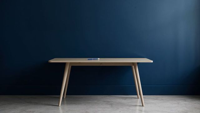 Minimal light wood table against deep navy wall with blue silver pen on concrete floor