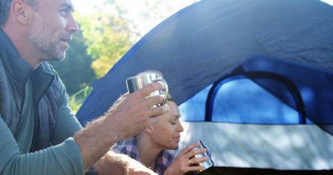 Middle-Aged Couple Relaxing with Warm Drinks by Camping Tent