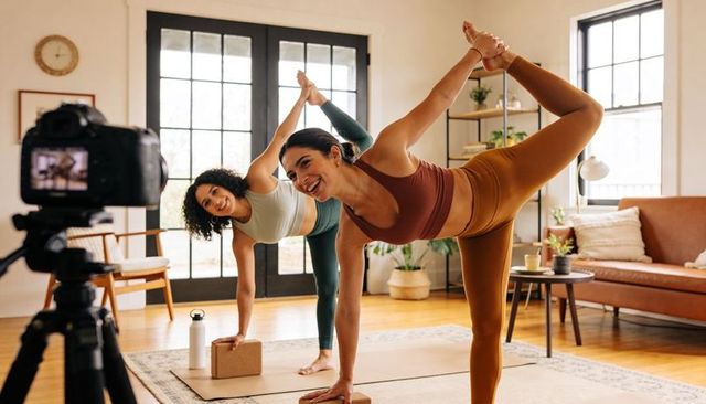 Women recording home yoga class practicing standing bow balance together with dslr camera