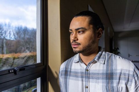Young man gazing out window, contemplative portrait in natural light, indoor corridor