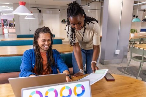 Diverse coworkers collaborating over laptop and printed charts in modern coworking space