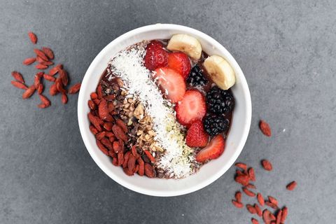 Serving vibrant acai bowl bursting with strawberries, blackberries, banana, coconut and goji berries