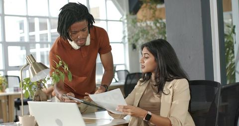 Indian woman collaborating with colleague over laptop in modern open-plan office