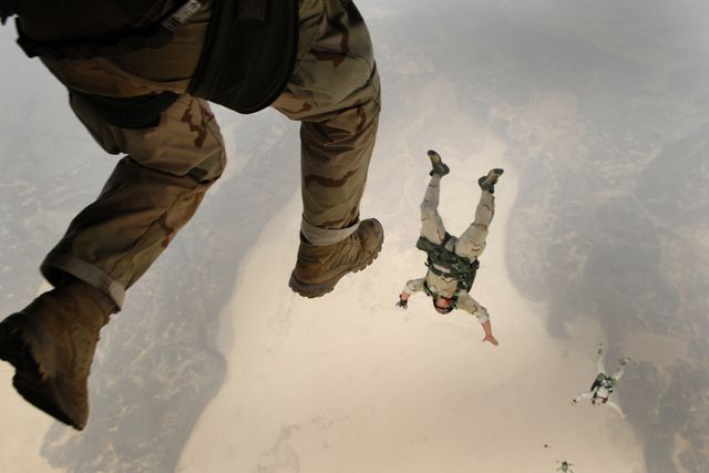 Paratroopers engaging in a high-altitude jump over a sprawling desert environment. Suitable for use in content related to military operations, extreme sports promotions, adventure advertisements, or team-building events.