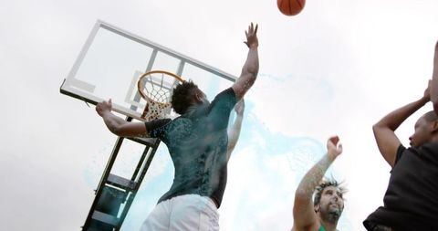 Jumping athlete reaching for basketball over rim at outdoor urban court during pickup game