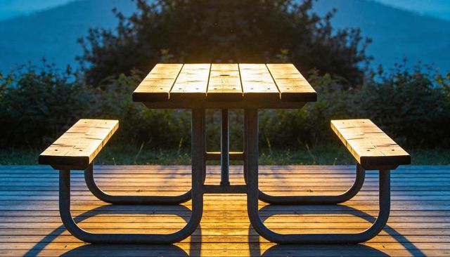 Golden sunrise bathing wooden picnic table with curved metal benches on deck