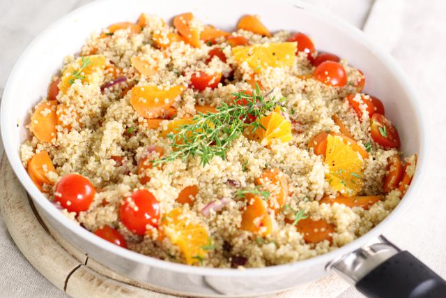 Bright, healthy vegetable and quinoa salad shown in a pan, perfect for meal preparation, recipes, healthy eating blogs, and culinary presentations. Featuring fresh cherry tomatoes, orange slices, sliced carrots, and garnished with herbs, this salad captures the essence of nutritious and tasty plant-based meals.