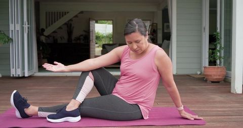 Mature woman performing seated spinal twist on home patio for gentle yoga workout