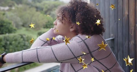 Contemplative young woman leaning on balcony railing with golden star overlay
