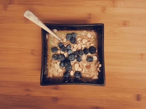 Serving warm oatmeal topped with fresh blueberries and sliced almonds in square ceramic bowl