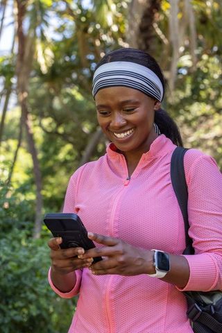 Smiling african woman checking smartphone after outdoor workout wearing pink athletic top