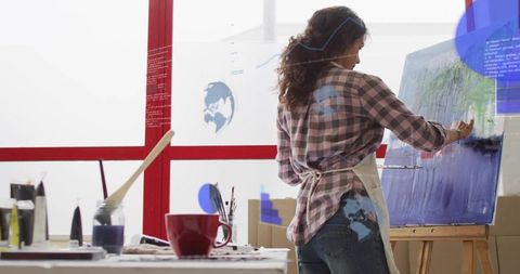 Woman Artist Painting Abstract Landscape on Easel in Bright Studio Wearing Plaid Apron