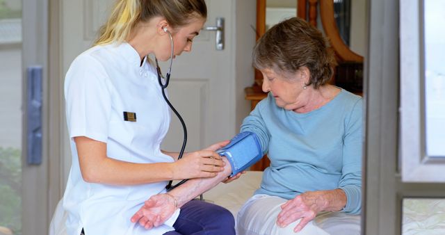 A young Caucasian female nurse is checking the blood pressure of a senior Caucasian woman, with copy space. Routine health check-ups like this are essential for monitoring and maintaining the well-being of elderly patients.