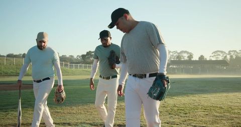 Teammates Walking Across Baseball Field at Sunrise Carrying Gloves and Bat