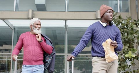 Intergenerational African American travelers waiting with rolling luggage at glass entrance