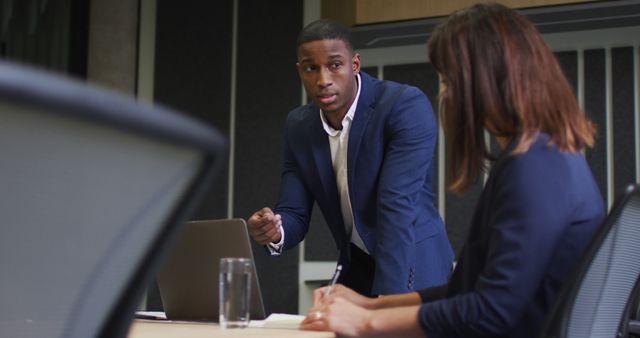 Male professional leading a discussion with a female colleague in a modern office environment. Perfect for showcasing teamwork, professional collaboration, and business planning in a corporate setting. Ideal use in business presentations, management training materials, and corporate websites.