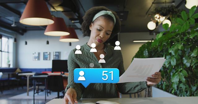 Image of profile icon floating over african american woman reading documents at office. Social media networking and business technology concept