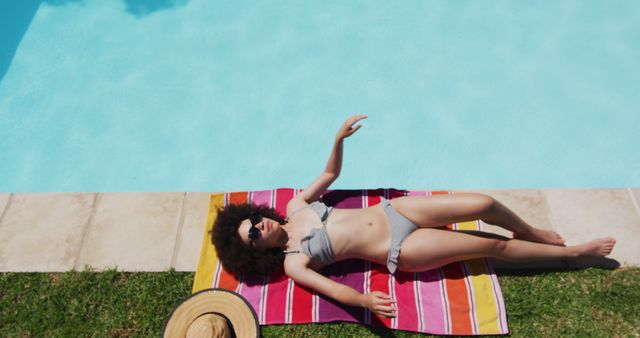 Biracial woman lying on blanket sunbathing by the pool. hanging out and relaxing outdoors in summer.