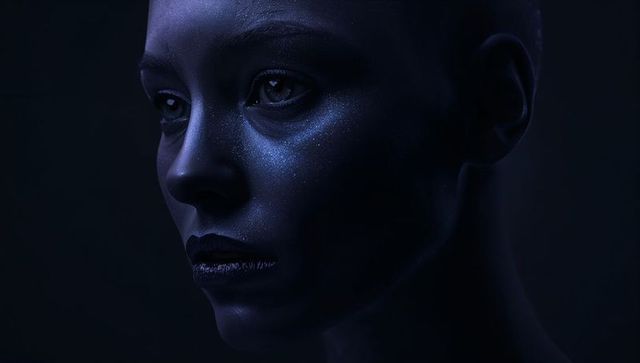Moody blue portrait of bald woman with glittered cheeks and dark lipstick, futuristic beauty