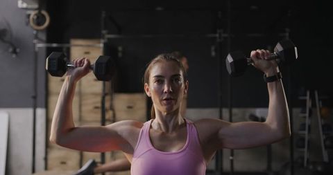 Focused woman lifting dumbbells in gym environment