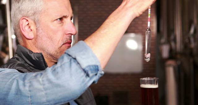 Mature man conducting a gravity test on beer using a hydrometer in a brewery. This image is perfect for use in brewing industry articles, beer production guides, or home brewing blogs emphasizing the importance of quality control and precision in the brewing process.