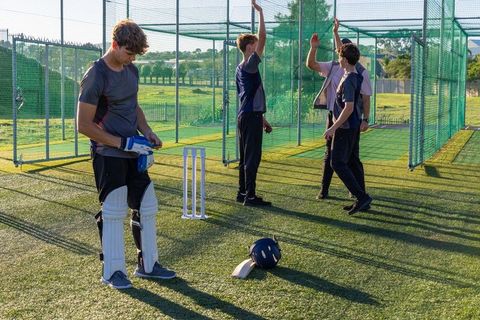 Diverse young cricket players practicing in nets, batter adjusting gloves and pads