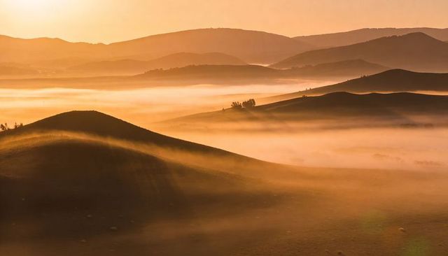 Golden sunrise mist rolling over sand dune and low hills creating layered amber landscape