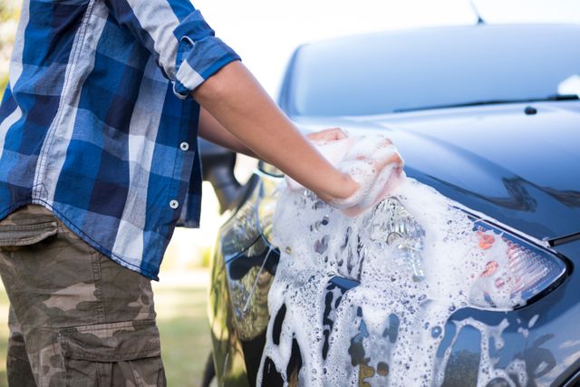 Mid-section of teenage boy washing a car 