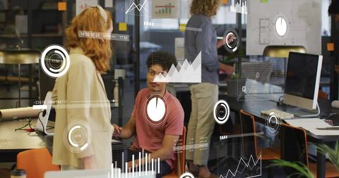 Young professionals collaborating at open office with data visualization on glass partition
