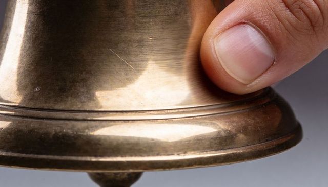 Fingertip tapping antique brass bell rim showing patina, scratches and reflections