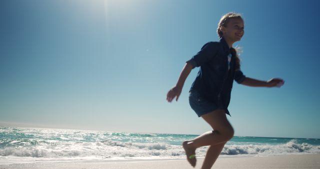Young girl is running on beach under bright sunlight. Ocean waves and clear sky highlight fresh, joyful moment. Ideal for ads related to family vacations, outdoor fun, summer activities, children's happiness.