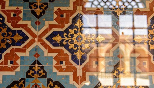 Ornate geometric ceramic tile panel featuring gold filigree and window reflection