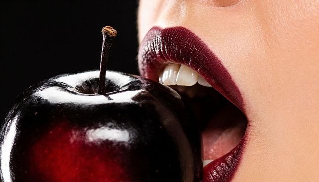 Biting glossy dark red apple with burgundy lips closeup beauty concept