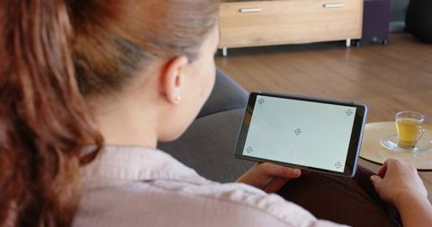 Woman holding tablet on sofa calibrating touchscreen with crosshair markers living room