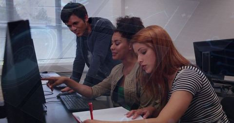 Three young adults collaborating at computer lab pointing at monitor and taking notes