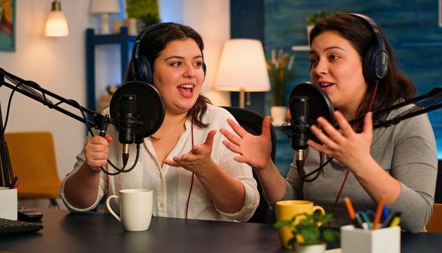 Hispanic women hosting energetic podcast in cozy studio, collaborating with microphones