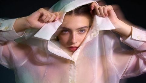 Female model pulling sheer shirt collar over head creating pastel translucent portrait