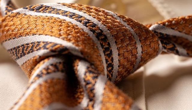 Woven golden-orange silk tie knot with silver-gray and navy stripes, macro texture detail