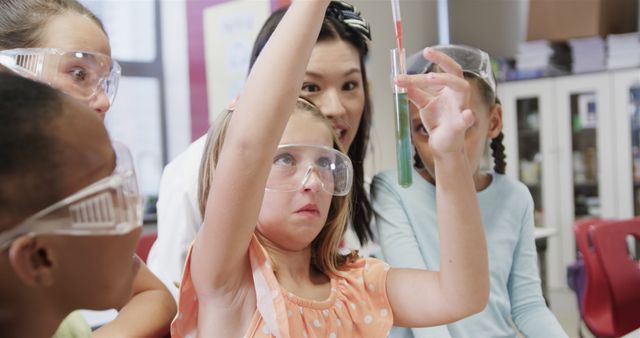 Group of elementary students wearing safety goggles and conducting a chemistry experiment with their teacher in a classroom. The students are engaged and focused on the task, showcasing their curiosity and collaborative learning. Perfect for content related to science education, classroom activities, teamwork, and inspiring young minds in STEM fields.