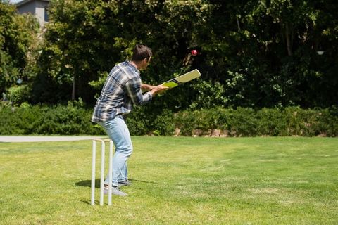 Man Playing Cricket on Sunny Day in Green Backyard